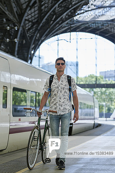 Mann schiebt Fahrrad durch einen Bahnhof