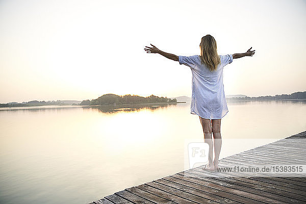 Rückansicht einer reifen Frau  die bei Sonnenaufgang auf einem Steg an einem See steht