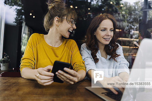 Two female friends with laptop and cell phone in a cafe