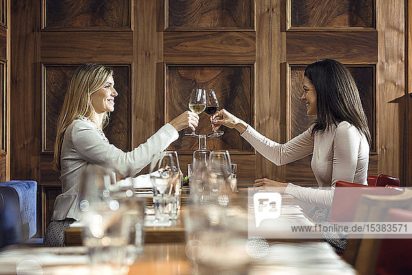 Zwei Geschäftsfrauen klirren in einem Restaurant an einem Weinglas