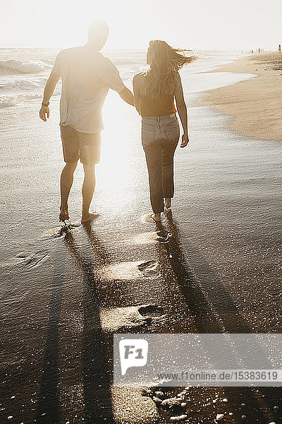 Zärtliches junges Paar beim Spaziergang am Meeresufer bei Sonnenuntergang