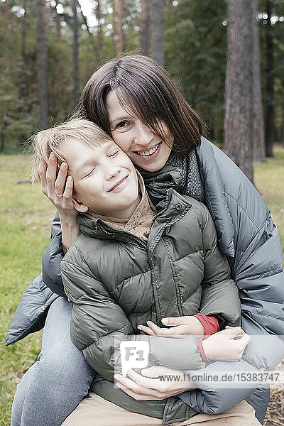 Mutter umarmt lächelnden Sohn in einem Park