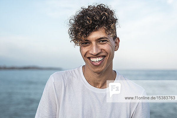Porträt eines lachenden jungen Mannes mit lockigem Haar am Meer