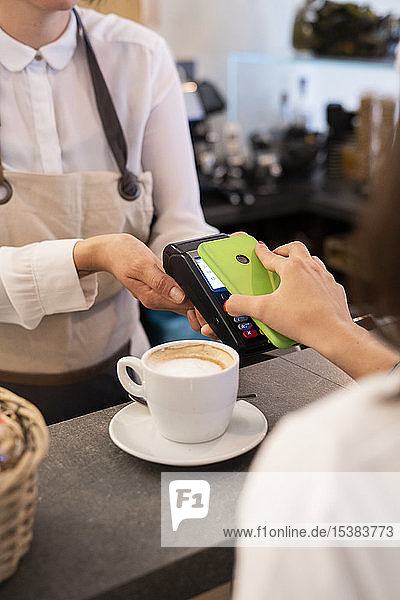 Close-up of customer paying cashless with smartphone in a cafe