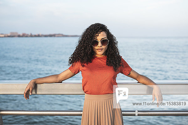 Beautiful woman  wearing sunglasses leaning on railing by the sea