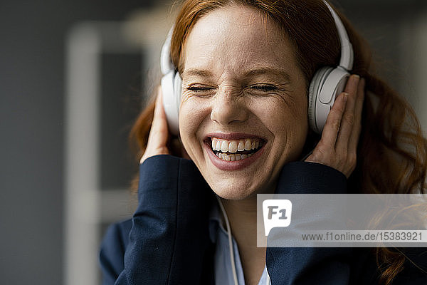 Porträt einer lachenden rothaarigen Geschäftsfrau  die mit weißen Kopfhörern Musik hört