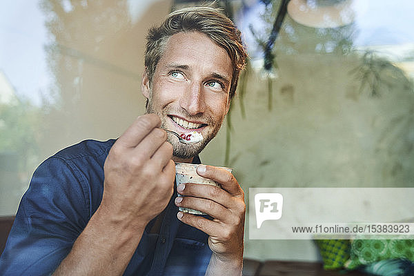 Porträt eines lächelnden jungen Mannes beim Müsliessen