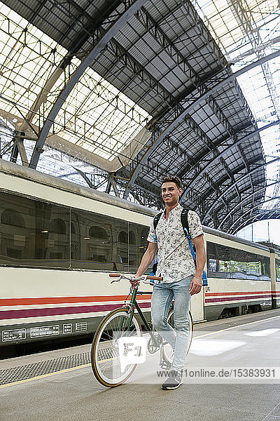Mann schiebt Fahrrad durch einen Bahnhof