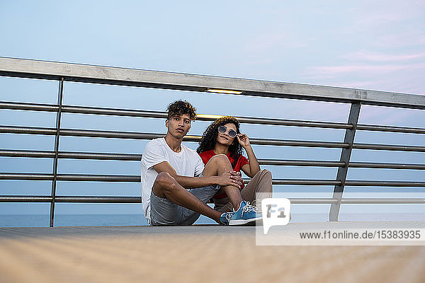 Junges Paar auf der Brücke am Meer sitzend
