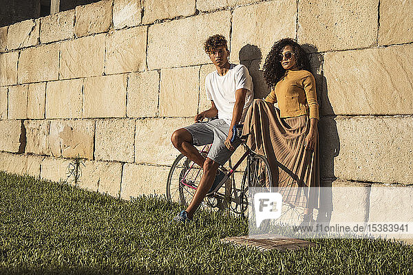 Young couple with bicycle  leaning on stone wall  looking cool