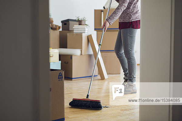 Woman sweeping the floor surrounded by cardboard boxes in an empty room
