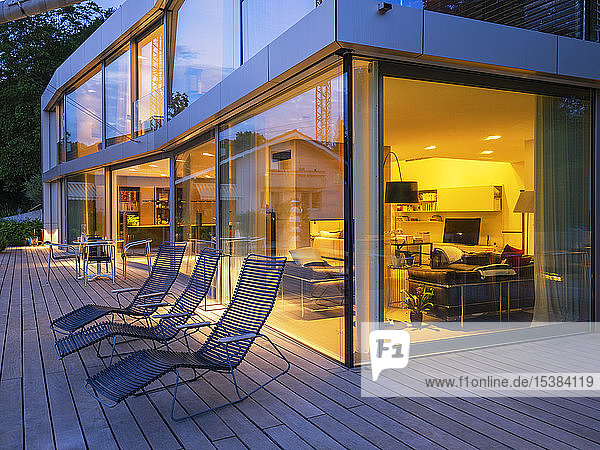 Schweiz  drei Liegestühle auf der Terrasse einer beleuchteten modernen Villa in der Abenddämmerung