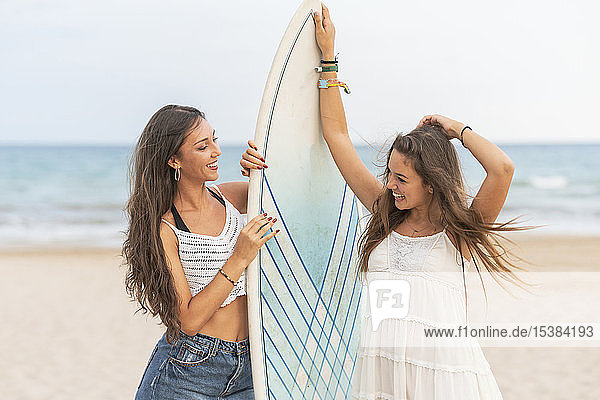 Zwei glückliche Freundinnen mit Surfbrett am Strand