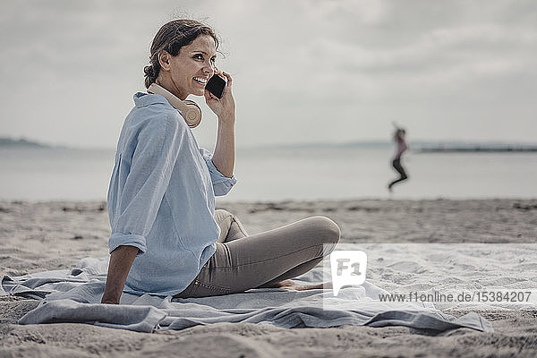 Frau sitzt am Strand und telefoniert