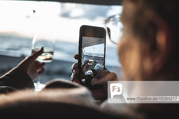 Frau fotografiert ein Glas Weißwein mit ihrem Smartphone am Strand