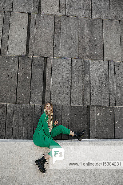 Blonde junge Frau in grünem Hosenanzug sitzt an einer Wand  Wien  Österreich