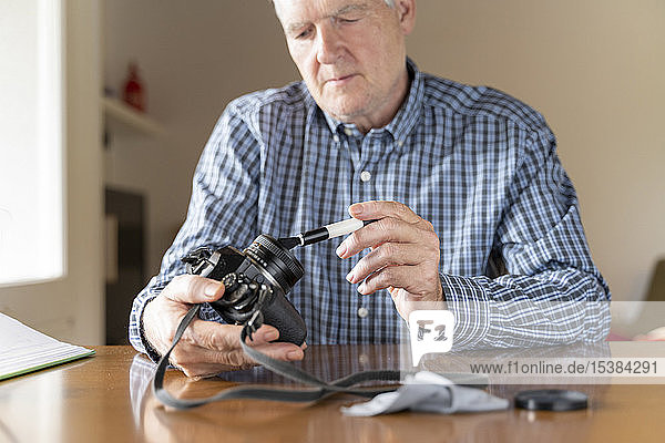 Seriöser Senior zu Hause reinigt Kamera