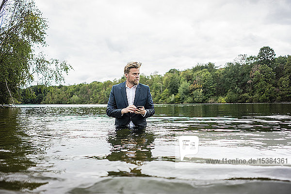 Businessman standing in a lake with cell phone
