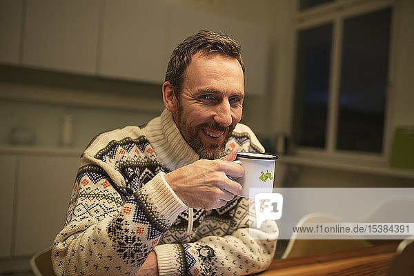 Portrait of happy casual businessman with mug sitting at table at home