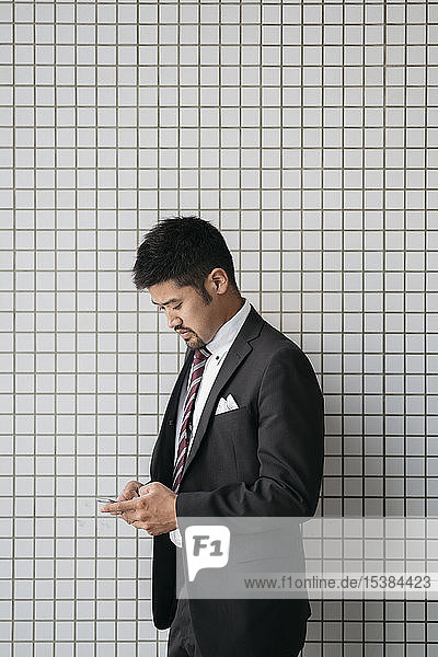 Junger Geschäftsmann benutzt Handy an gekachelter Wand