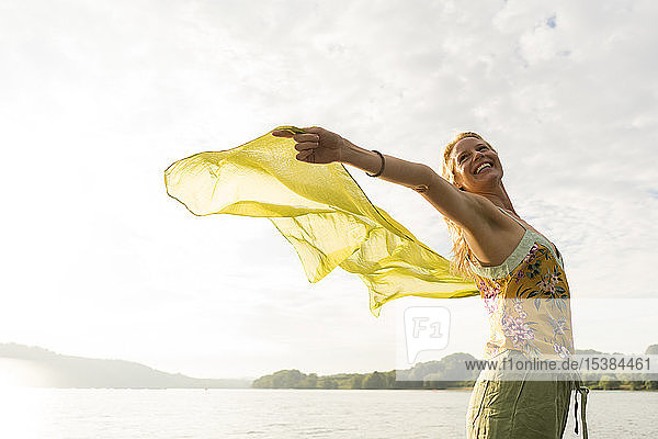 Glückliche junge Frau hält ein Tuch an einem See
