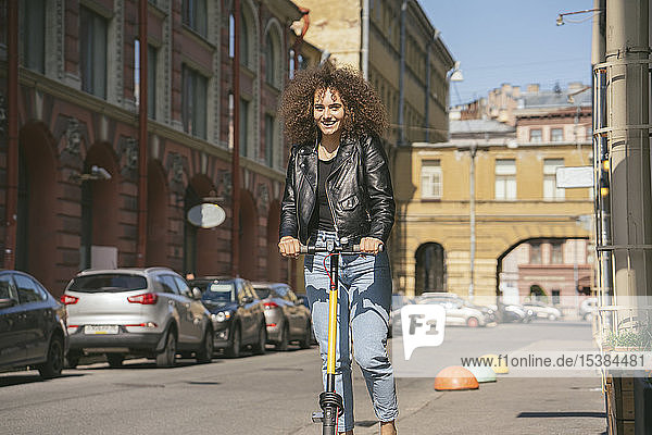 Porträt eines lächelnden Teenager-Mädchens auf einem Roller auf dem Bürgersteig