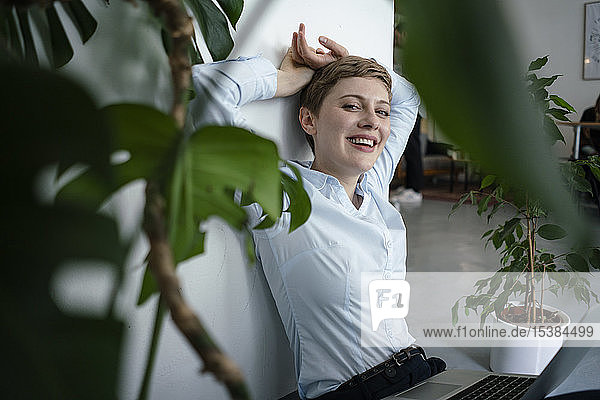 Porträt einer Geschäftsfrau mit Laptop auf dem Boden sitzend  umgeben von Pflanzen