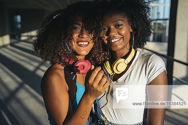 Porträt von zwei glücklichen jungen Frauen mit Kopfhörern in der Abenddämmerung