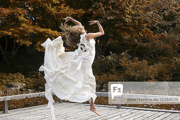Ballerina wearing white dress and jumping on wooden jetty