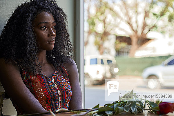 Porträt einer jungen afrikanischen Frau mit Blumen auf dem Tisch in einem Café  die aus dem Fenster schaut
