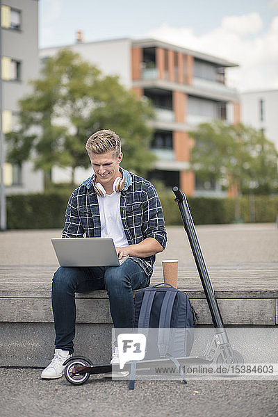 Young businessman with e-scooter using laptop in the city