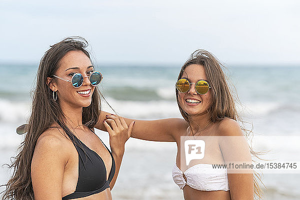 Two happy female friends wearing sunglasses on the beach