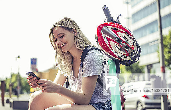 Lächelnde junge Frau mit E-Scooter schaut auf Handy  Berlin  Deutschland