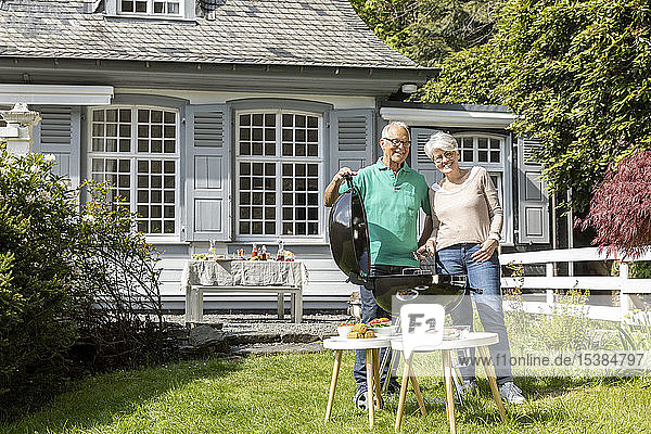 Glückliches älteres Ehepaar beim Grillen im Garten ihres Hauses