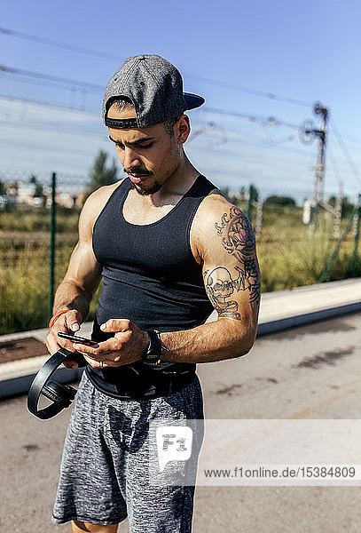 Sporty young man with smartphone and headphones standing on a road