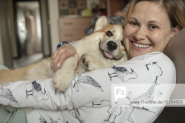 Porträt einer glücklichen Frau  die zu Hause mit ihrem Hund kuschelt