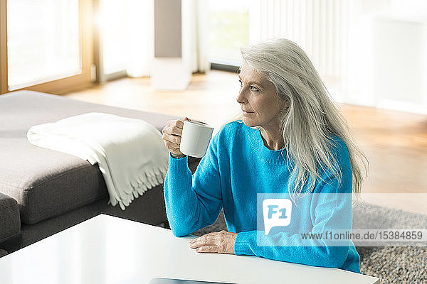 Nachdenkliche reife Frau mit einer Tasse Kaffee zu Hause  die in die Ferne schaut