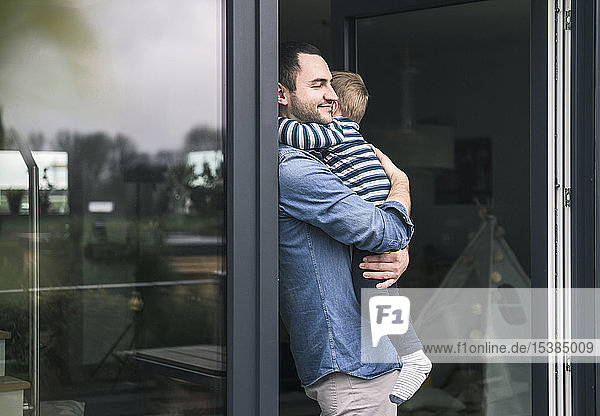 Vater umarmt Sohn an Terrassentür zu Hause