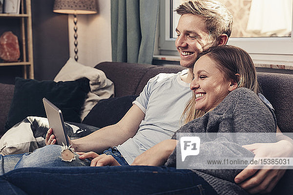 Glückliches junges Paar mit Tablette auf der Couch zu Hause
