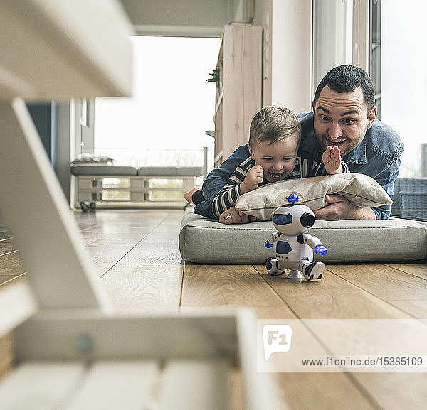 Excited father and son lying on a mattress at home watching a toy robot