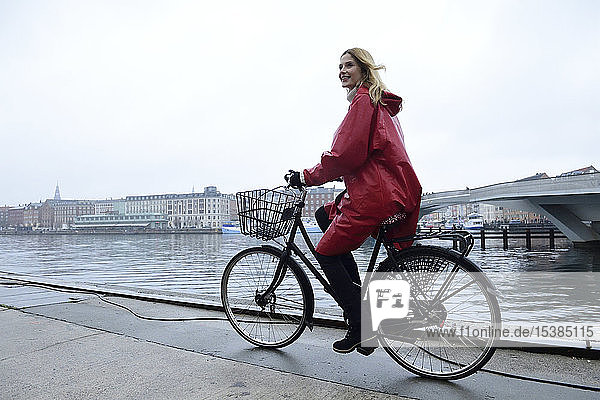 Dänemark  Kopenhagen  glückliche Frau fährt bei Regenwetter mit dem Fahrrad an der Uferpromenade