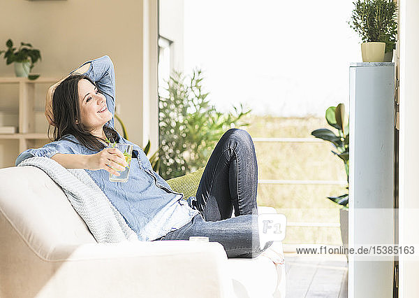 Glückliche Frau mit einem Glas aufgegossenem Wasser  die zu Hause auf der Couch sitzt
