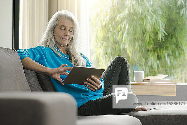 Portrait einer reifen Frau  die zu Hause auf der Couch sitzt und ein digitales Tablet benutzt
