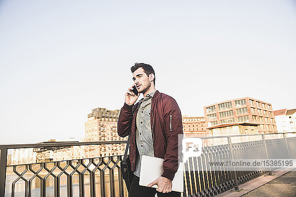 Young man with tablet talking on cell phone on a bridge in the city