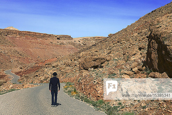 Morocco  Ounila Valley  rear view of man wearing a bowler hat standing on road in the mountains