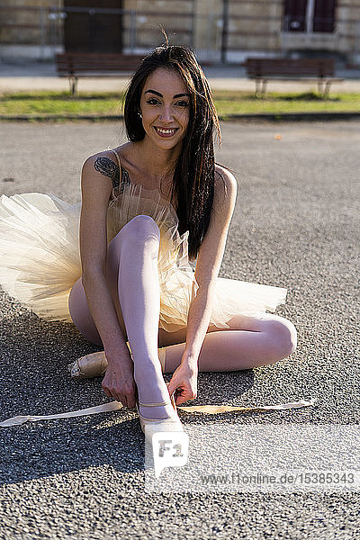 Italien  Verona  Porträt einer lächelnden Ballerina  die in der Stadt sitzt und Ballettschuhe anzieht