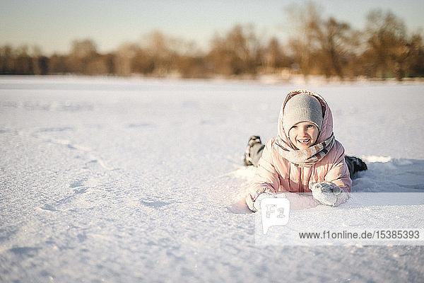Portrait of little girl lying in snow field