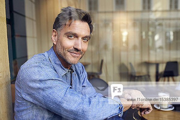 Porträt eines selbstbewussten Mannes hinter einer Fensterscheibe in einem Cafe