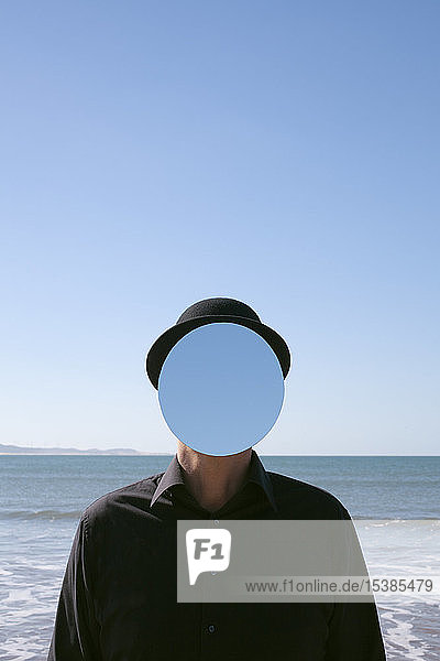 Morocco  Essaouira  man wearing a bowler hat with mirror in front of his face at the sea