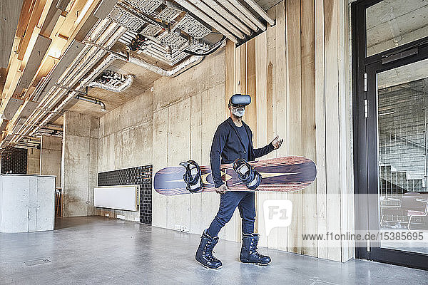Älterer Geschäftsmann mit VR-Brille hält Snowboard in modernem Büro
